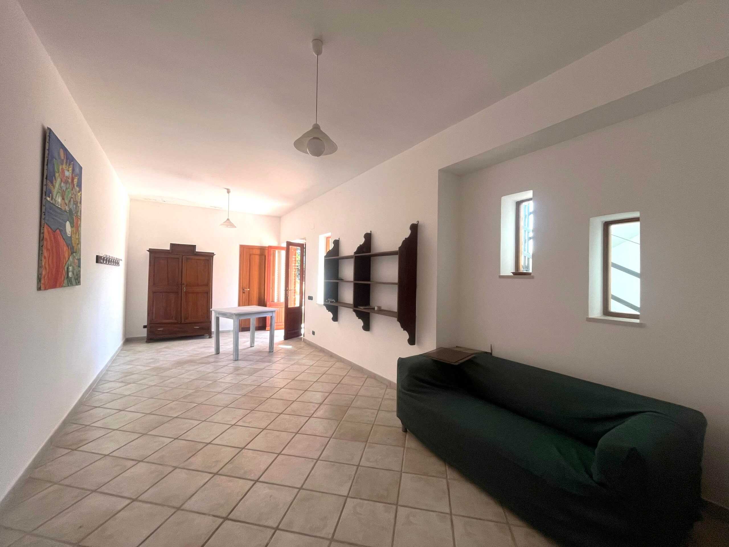 Ampio soggiorno arredato con divano verde, pareti bianche, piccole finestre e mobili in stile classico, ideale per vivere spazi luminosi e accoglienti nella tua casa.