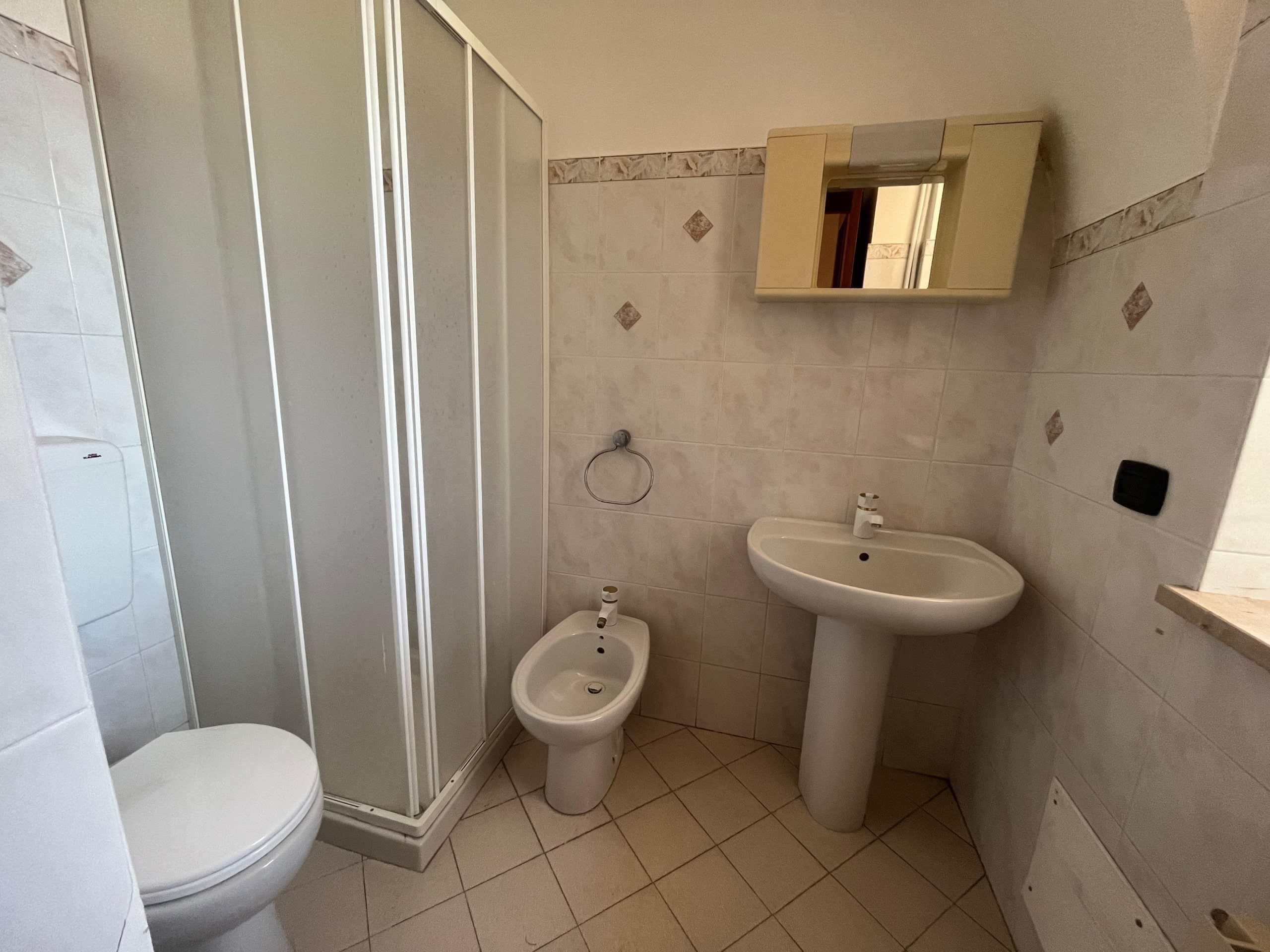 Doccia bagno con rubinetto bianco e specchio con mobiletto incassato, ambiente con piastrelle chiare, lavabo con basamento, elemento funzionale e pratico per spazi bagno.