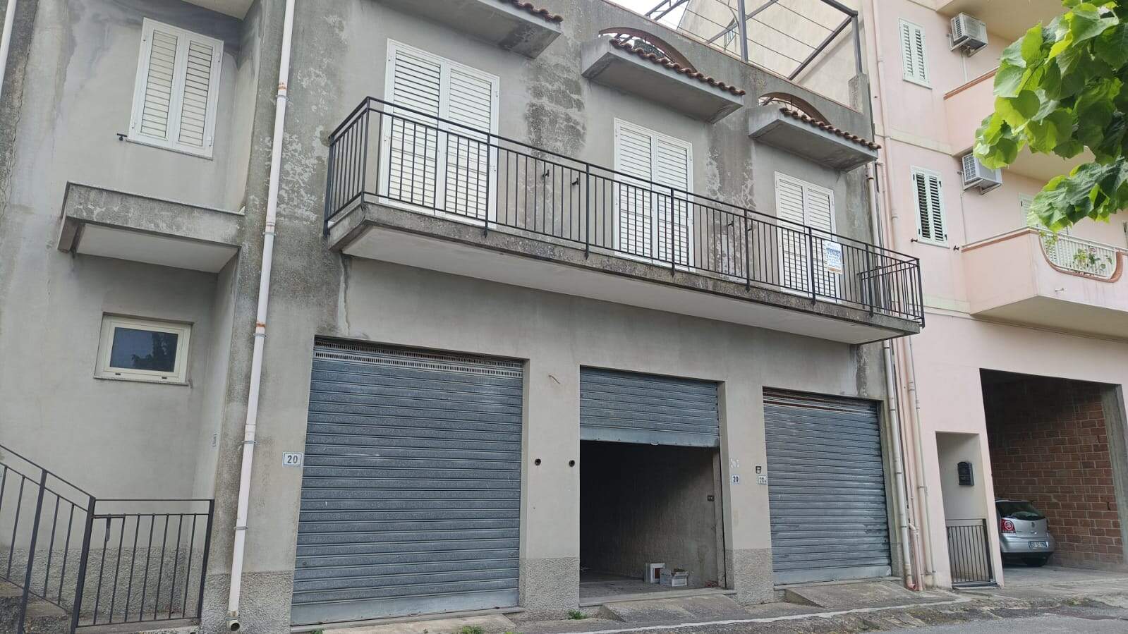 Finestra, balcone e garage di un edificio residenziale antico con facciata in stucco, ristrutturazione e serrande avvolgibili, in un contesto urbano di Napoli, Italia.