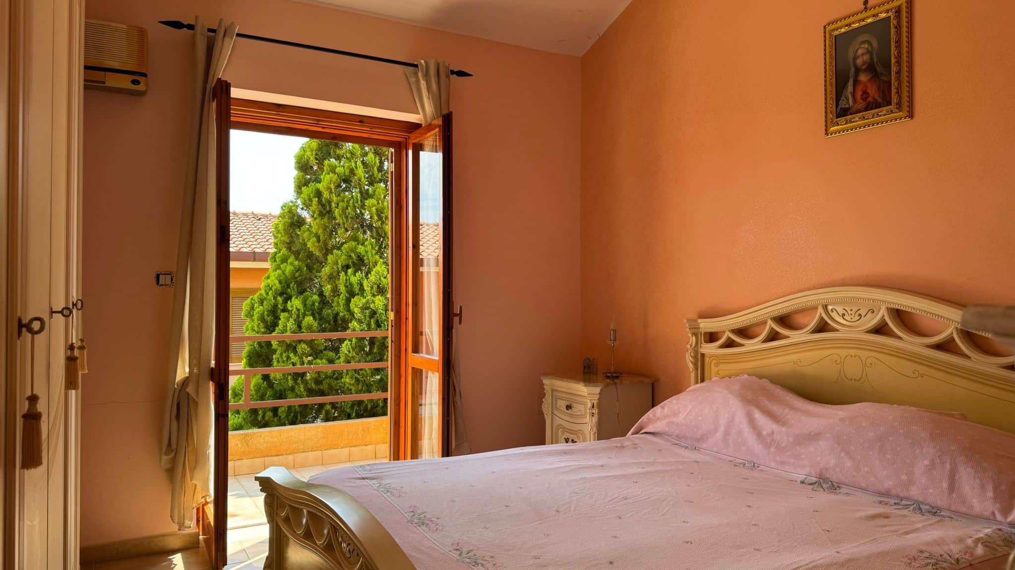 Balcone e camera da letto con mobili classici in stile romantico, pareti color pesca e vista su un albero verde.