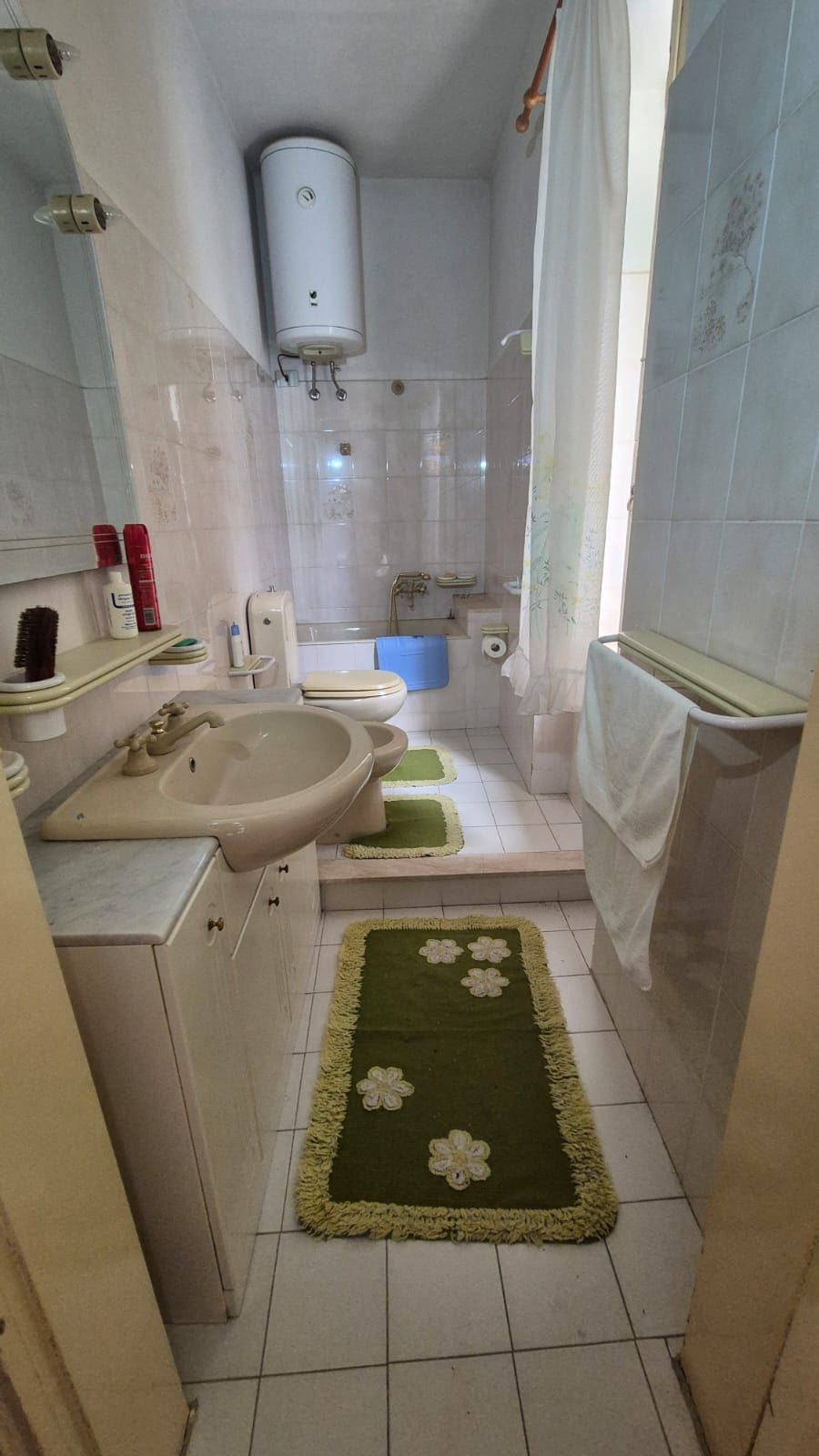 Lavabo e bagno completo in un appartamento con accessori eleganti e pratici, piastrelle chiare e tappeti verdi floreali, ideale per soggiorni confortevoli e funzionali.