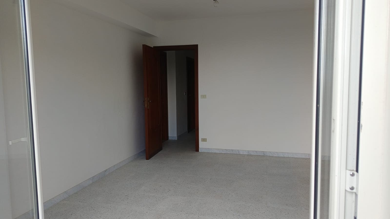 Spazio vuoto in appartamento con pareti bianche e porta in legno, ambiente luminoso e accogliente, ideale per casa moderna o investment immobiliare.