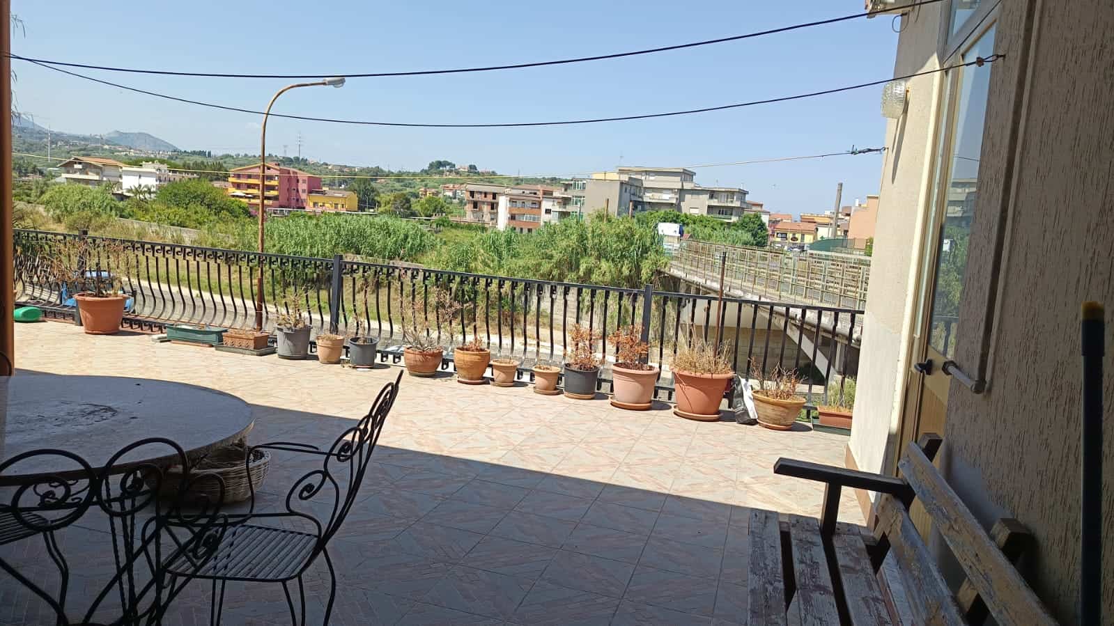 Luminoso terrazzo con vista su zona residenziale e natura, ideale per relax e cene all'aperto, con piante in vaso e arredi in stile classico, perfetto per vivere all'aperto.