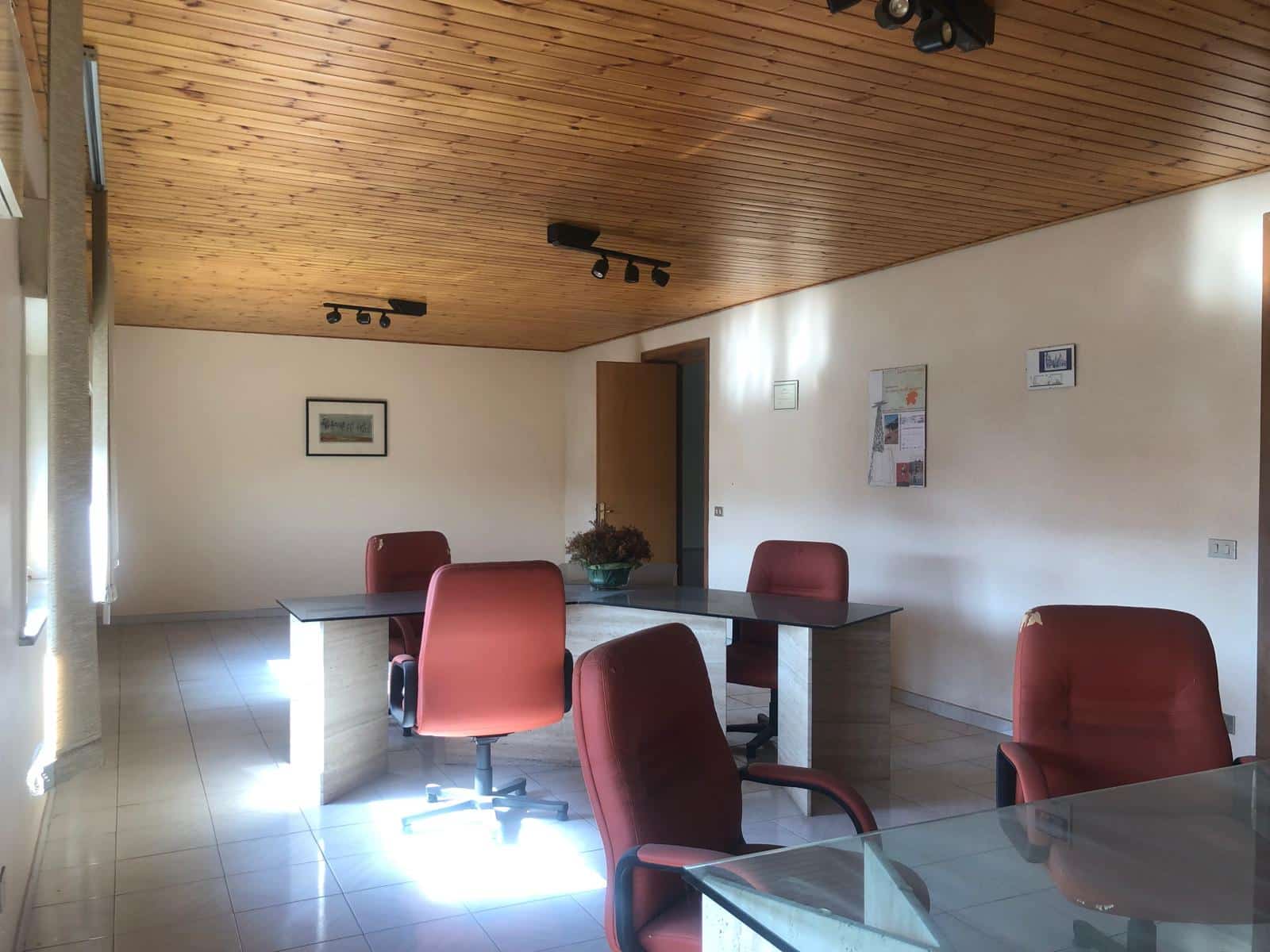 Spazi di lavoro in ufficio moderno con tavoli e sedie ergonomiche, illuminazione naturale e soffitto in legno, ideali per ambienti aziendali produttivi e accoglienti.