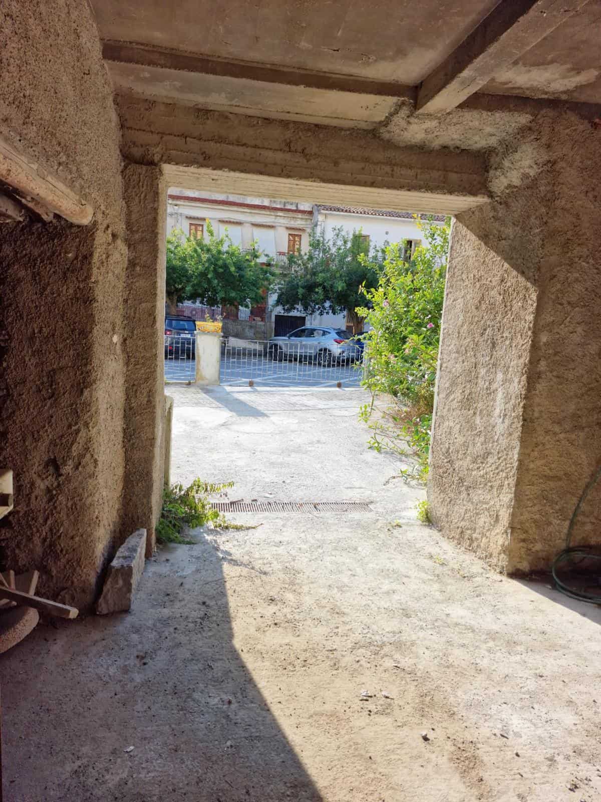 Finestra su strada con alberi e case in stile tradizionale, vista dallo spazio interno di un edificio in costruzione o ristrutturazione, dettaglio architettonico rustico e naturale.