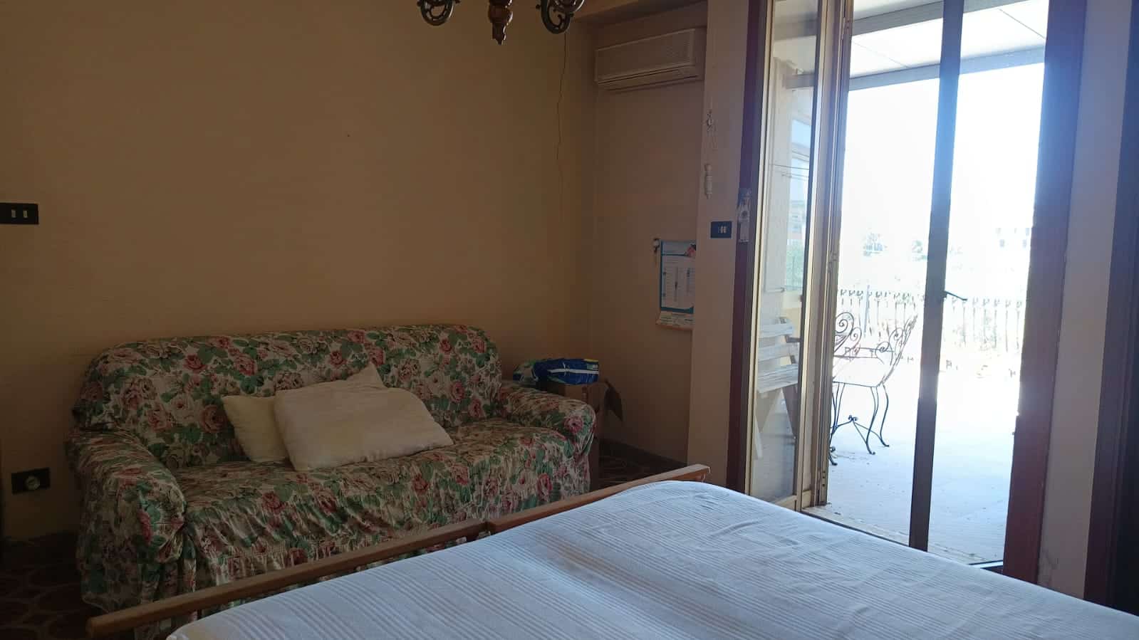 Immagine di un soggiorno con divano floreale e accesso a terrazza soleggiata, ideale per case vacanze e affitti a breve termine.