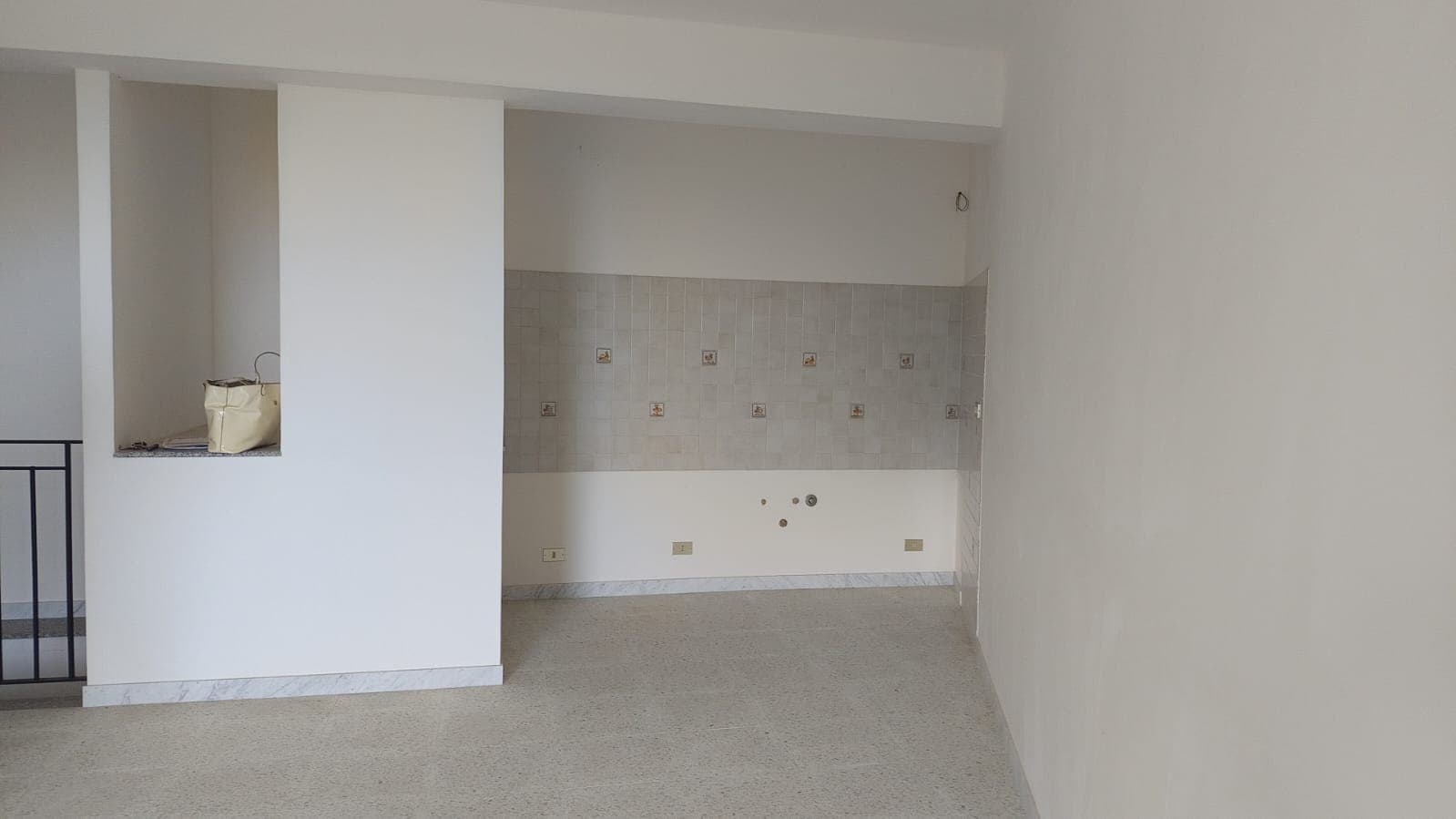 Finestra con vista su interni in fase di ristrutturazione, pareti bianche, pavimento in moquette beige, spazio living open space, cucina non ancora installata, immobile pronto per personalizzazione.