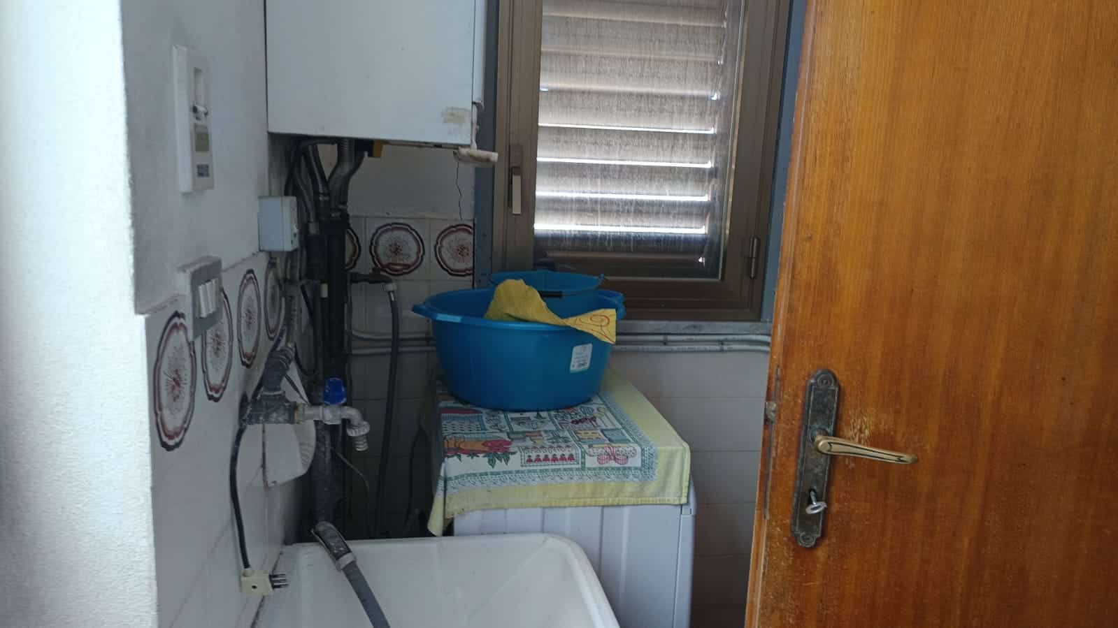 Lavanderia domestica con lavatrice e spazio per il bucato, finestra con tapparelle, arredamento semplice, ambiente funzionale e pratico, ideale per la gestione del bucato in casa NextCasa.