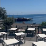 Frequente spiaggia con tavoli e sedie all'aperto, vista mare e barca, luogo ideale per mangiare e rilassarsi vicino al mare in una località balneare italiana.