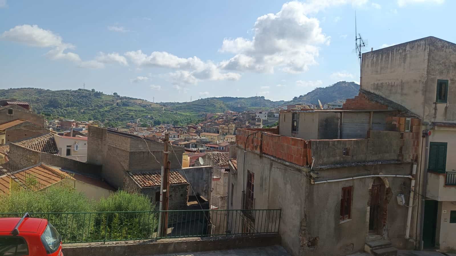 Villaggio storico con tetti in terracotta e case antiche, vista panoramica sulle colline verdi e il cielo soleggiato, tipico paesaggio urbano in Italia, ideale per acquisto e investimento immobiliare.