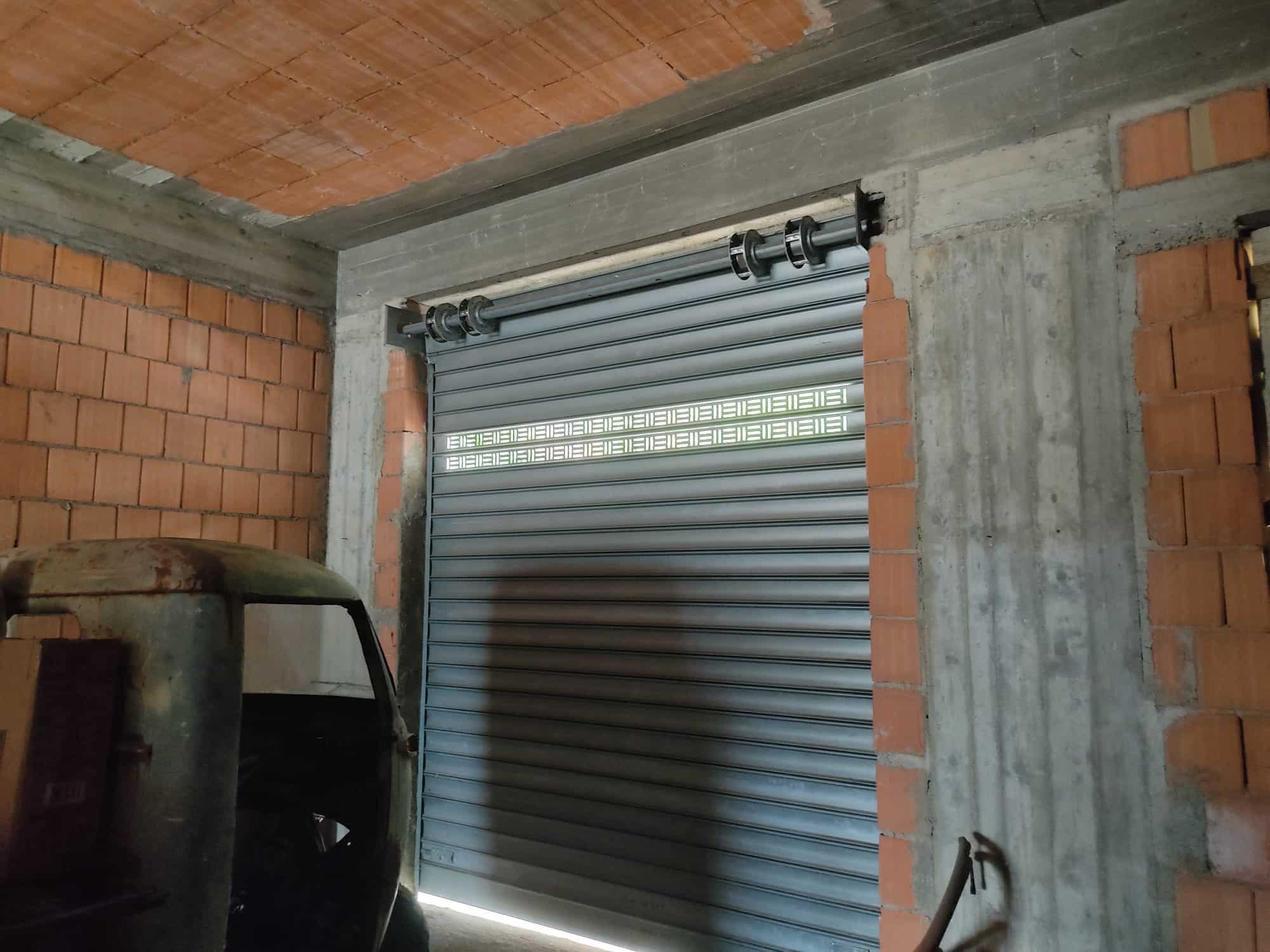 Finestra con porta basculante in garage in costruzione, muro in cemento e mattoni crudi, ambiente di lavoro edilizio.