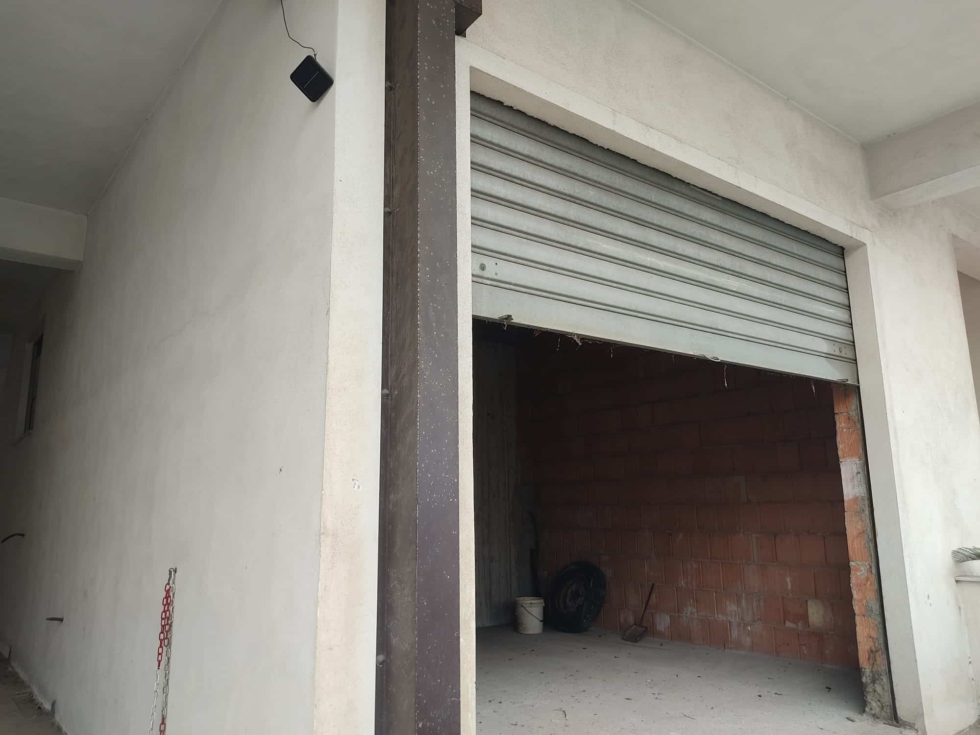 Finestra di garage in costruzione con serranda avvolgibile, muro isolato e spazio per parcheggio auto, pronto per essere completato con finiture e dettagli di design.