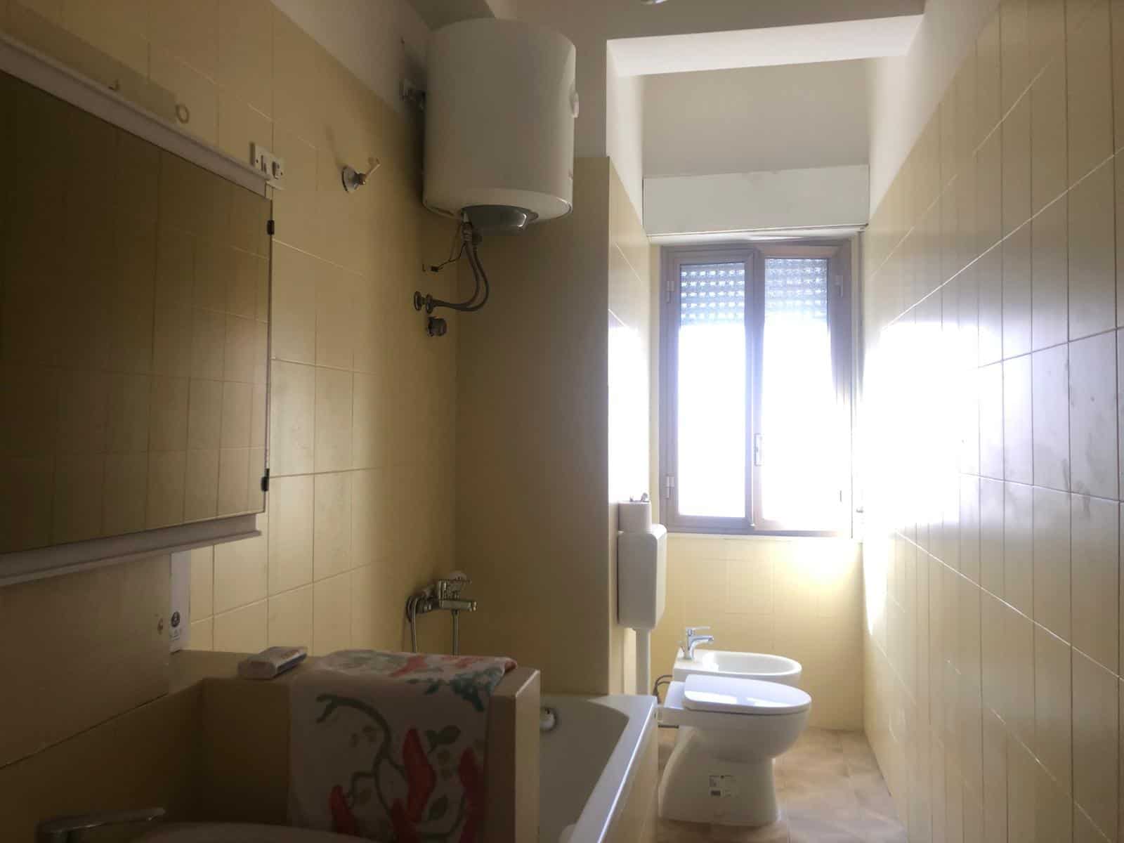 Bagno spazioso con grandi finestre, sanitari moderni, asciugatrice, lavabo e pareti piastrellate in stile semplice e funzionale.