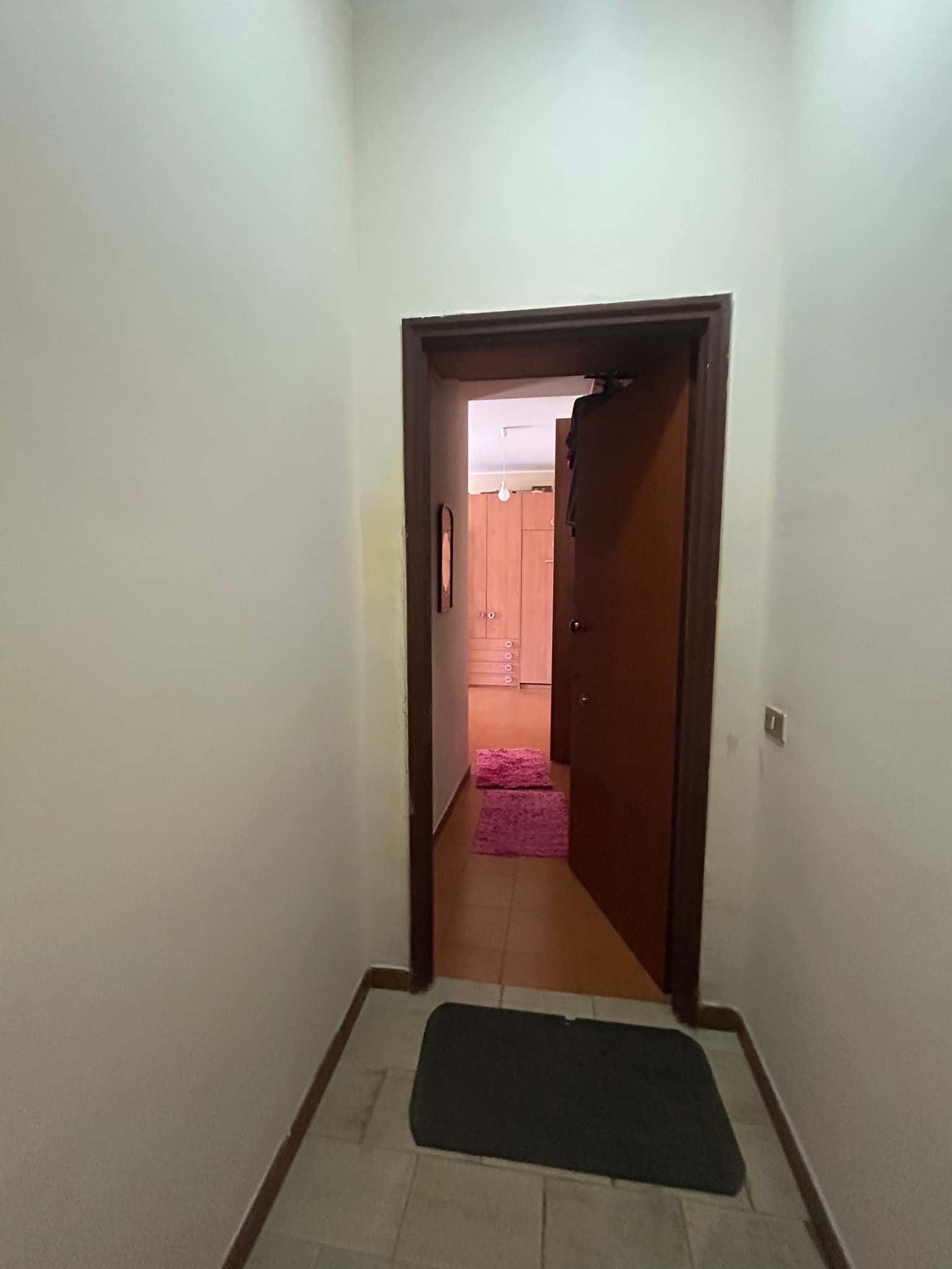 Porta d'ingresso di una casa o appartamento, vista dall'ingresso con pareti chiare, pavimento in ceramica e porta aperta verso il soggiorno o le camere.