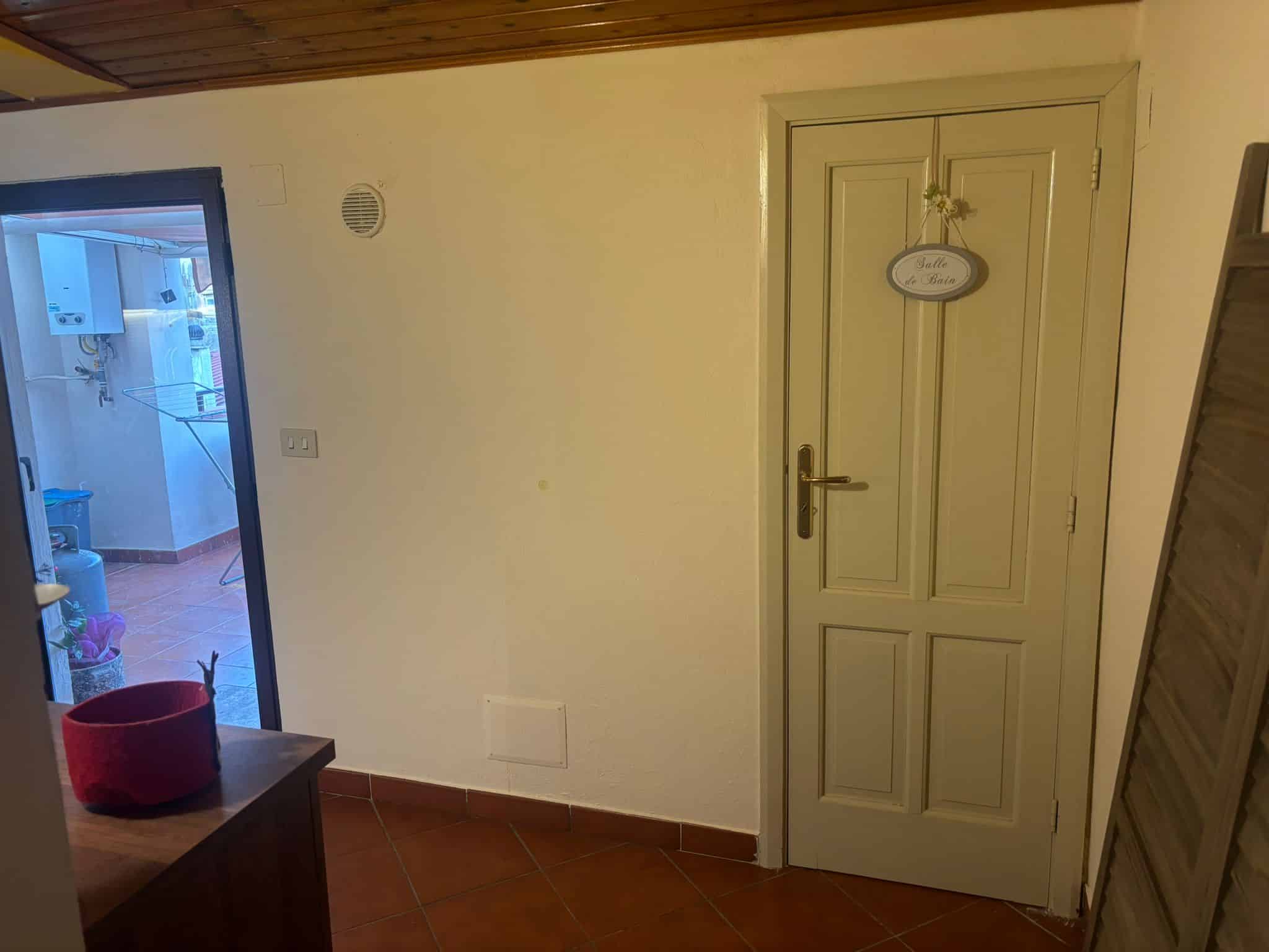 Lavanderia con porta a vetri che conduce al patio esterno, pavimento in terracotta e pareti gialle, zona funzionale ideale per gestione vestiti e stiro, arredamento semplice e pratico.