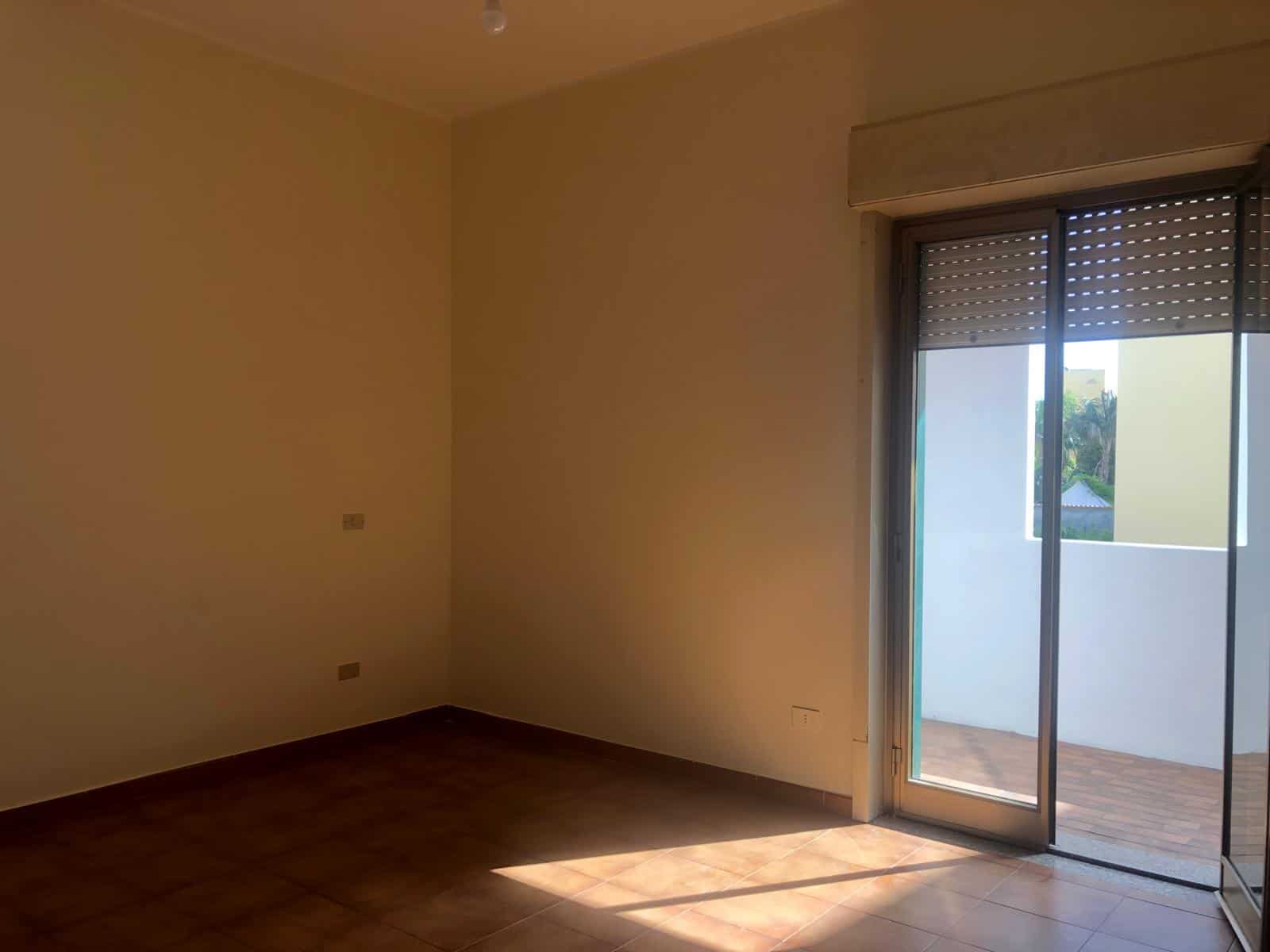 Finestra con porta scorrevole verso il balcone, stanza vuota con pareti beige e pavimento in ceramica, luce naturale che entra dalla porta, ideale per immobili residenziali moderni.