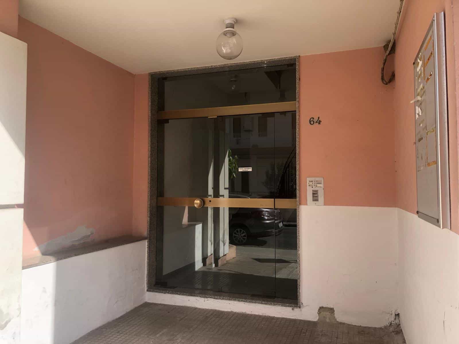 Ingresso condominiale con portoncino in vetro e numerazione 64, arredato con pareti rosa e bianca, area di accesso protetta e spazio per posta o annunci pubblicitari.