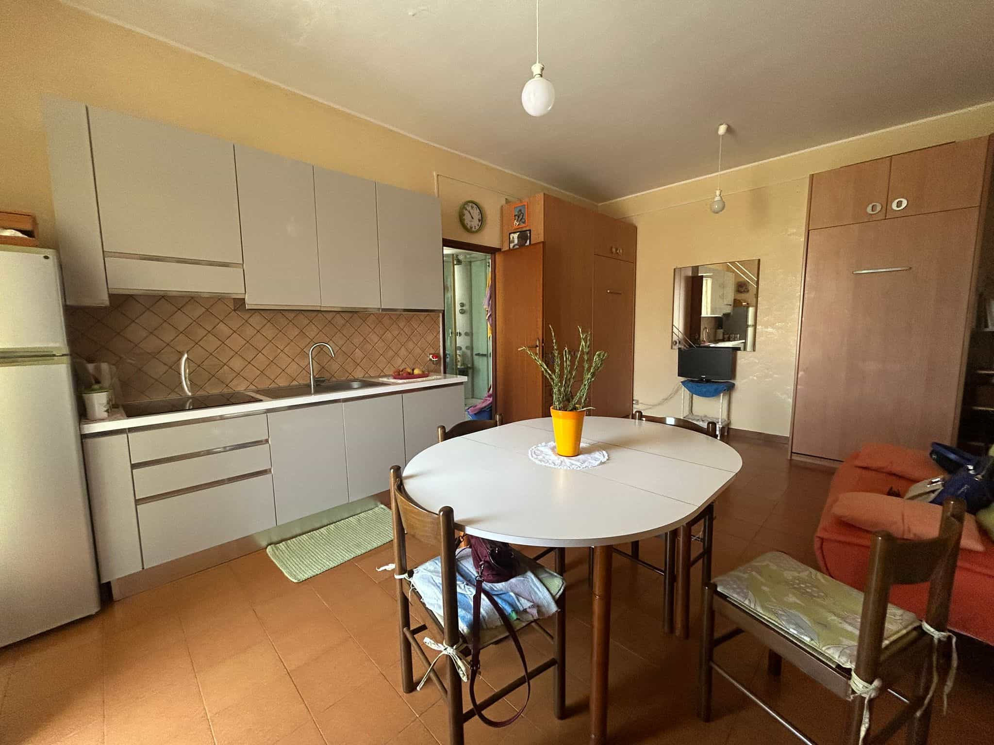 Finestra sulla cucina abitabile con mobili moderni e zona pranzo con sedie in legno e tovaglia, ambiente accogliente e funzionale.