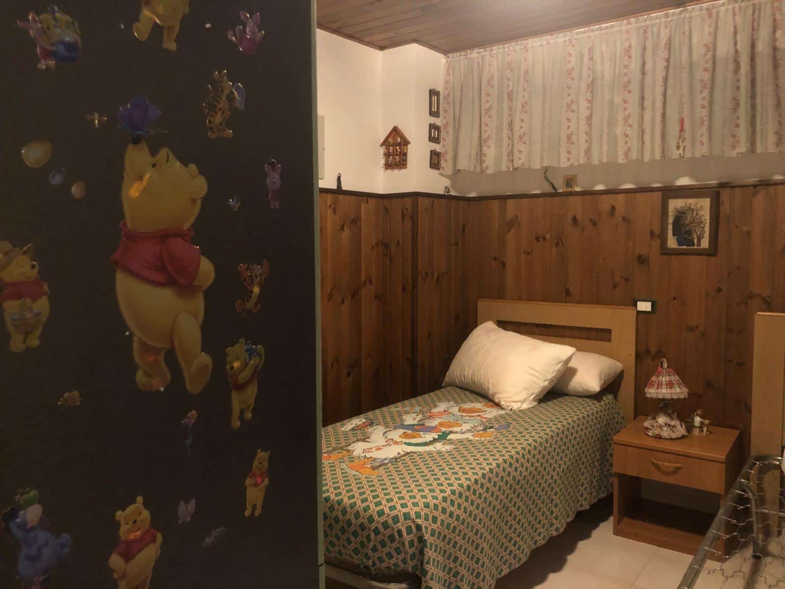 Winnie the Pooh stanza camera da letto, arredamento rustico con pareti in legno, letto singolo con copriletto decorato, lampada da tavolo e quadro su parete in stile tradizionale.