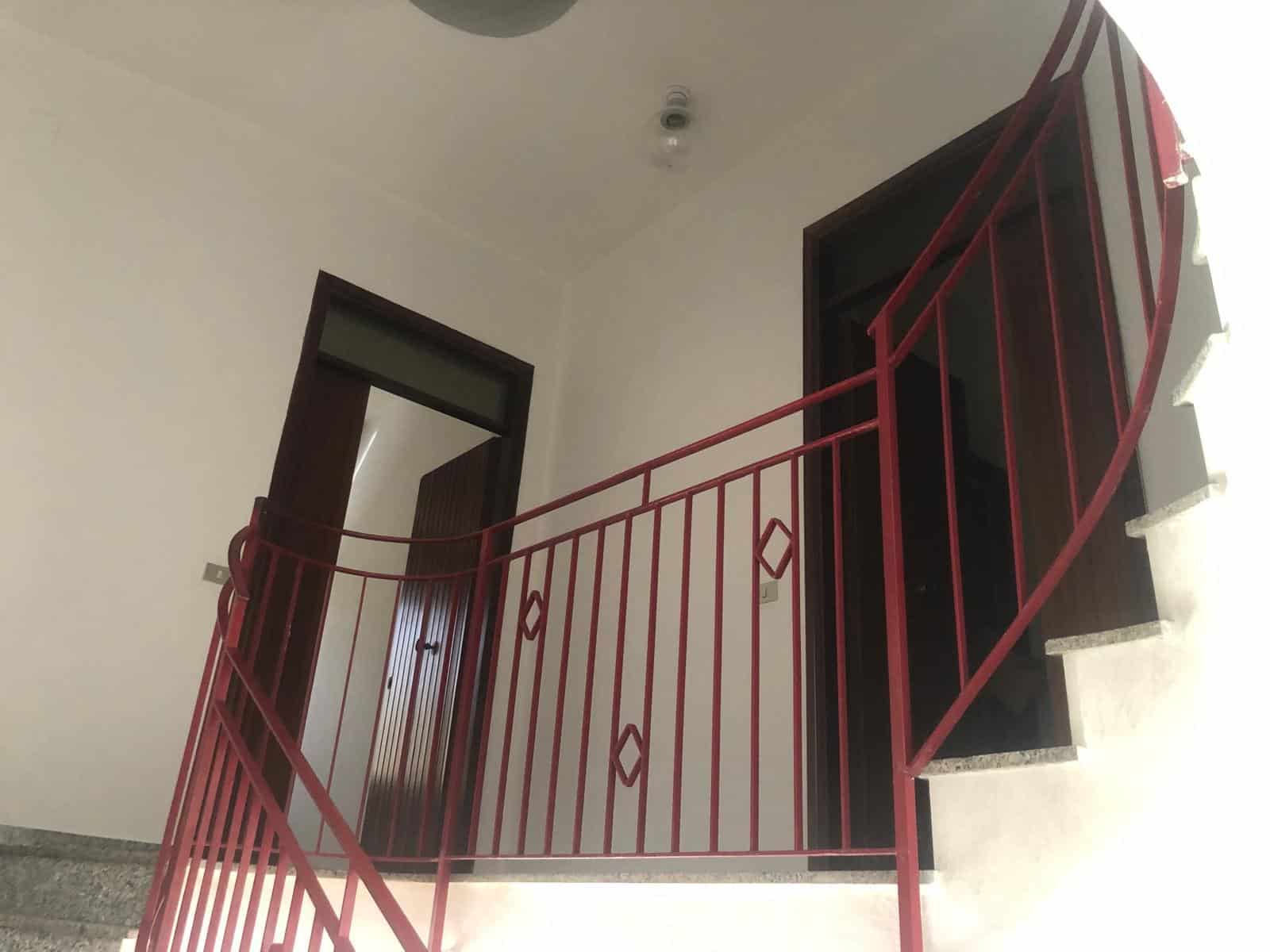 Scala interna con ringhiera rossa in ferro battuto, accesso a piano superiore, in un appartamento moderno, foto dagli interni casa NextCasa.