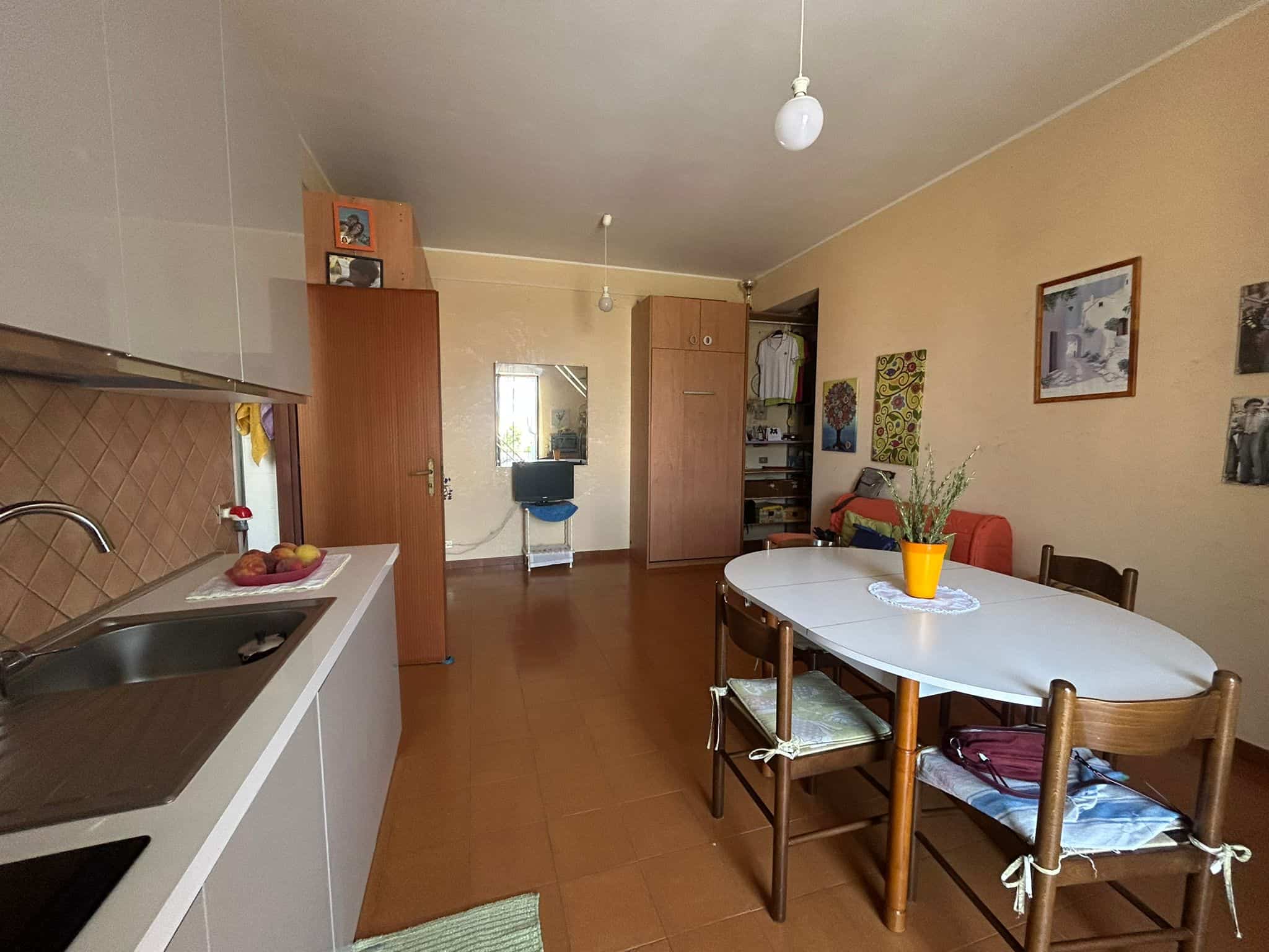 Ampio soggiorno con cucina abitabile, tavolo da pranzo, pareti decorate con quadri, mobili in legno, ambiente luminoso e accogliente, ideale per la vita quotidiana e momenti di convivialità.