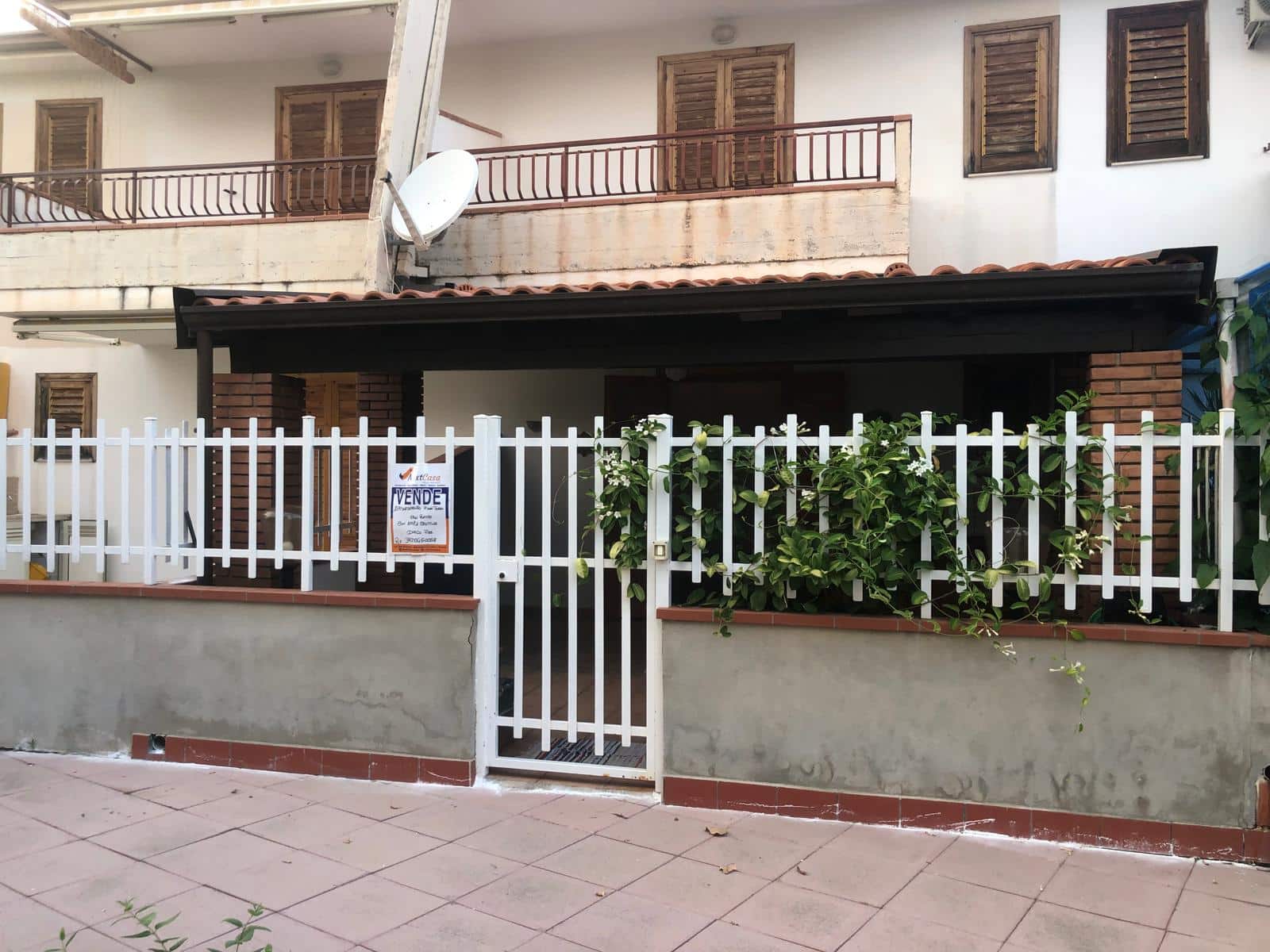 Cancello e recinzione in ferro bianco con vaso di piante, facciata di casa in vendita, immobile residenziale con giardino, stile moderno e funzionale.