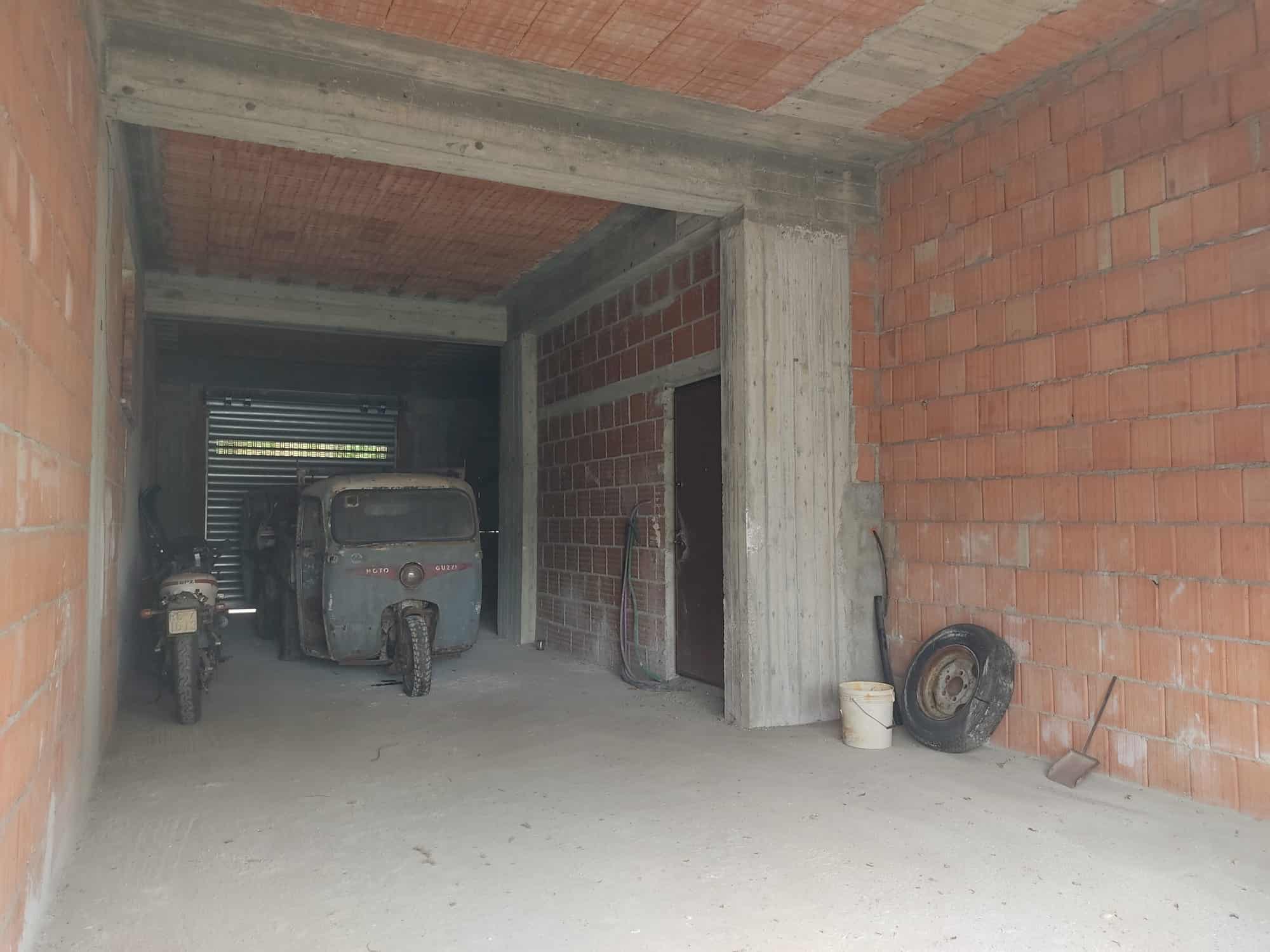 Motocicletta e veicolo d'epoca in garage in costruzione, con mattoni a vista e spazio ancora da terminare, parte di un progetto edilizio di NextCasa, specializzata in immobili e costruzioni.