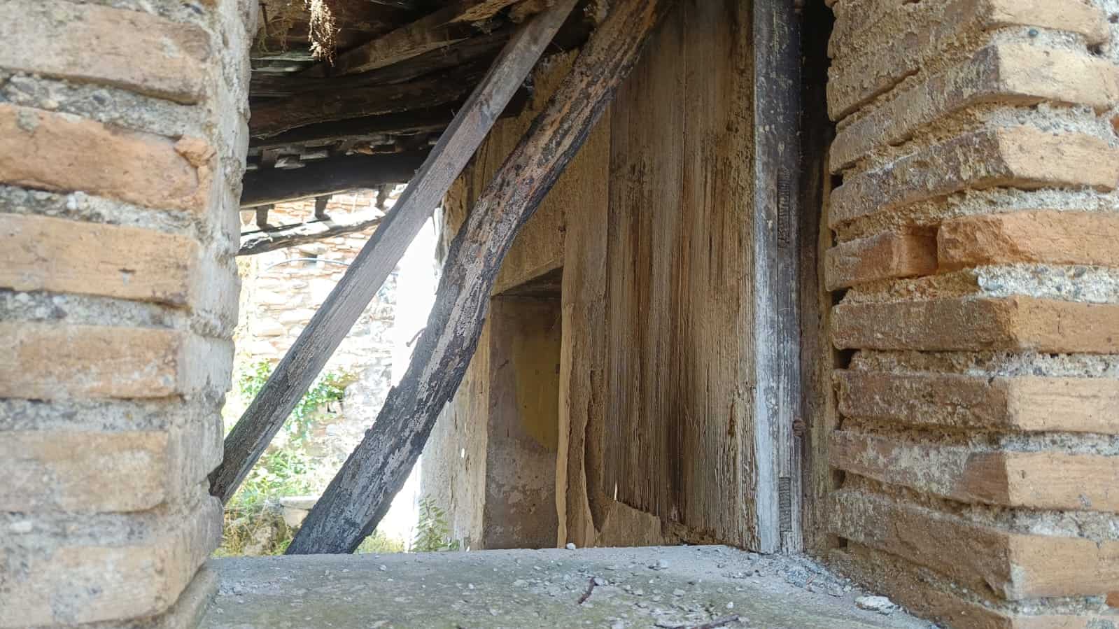 Vecchio muro in mattoni di cotto e pietra, dettaglio di un edificio in ristrutturazione o abbandonato, mostra la struttura in legno deteriorata, perfetto per immagini di restauro di case rustiche o storiche.