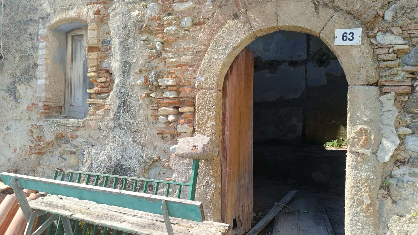 Vecchio portale in pietra e mattoni di un edificio storico in fase di restauro, con porta in legno e finestra in muratura, caratterizzato da un’atmosfera rustica e autentica, esempio di architettura tradizionale italiana.