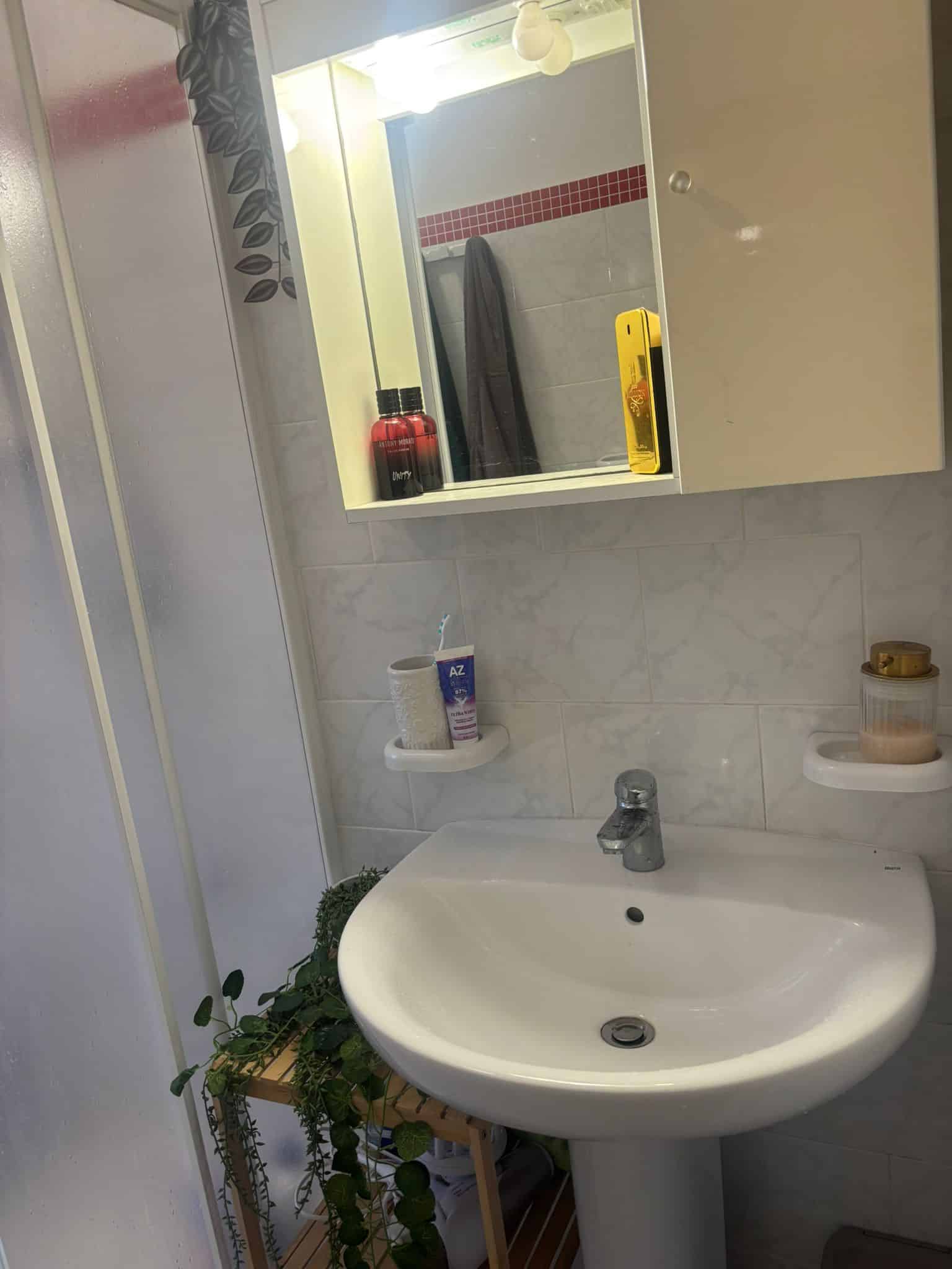 Lavabo bianco con specchio e armadietto in bagno, accessori bagno come portaspazzolino e shampoo, arredamento funzionale e pulito, ideale per ristrutturazione e progettazione di interni bagno.
