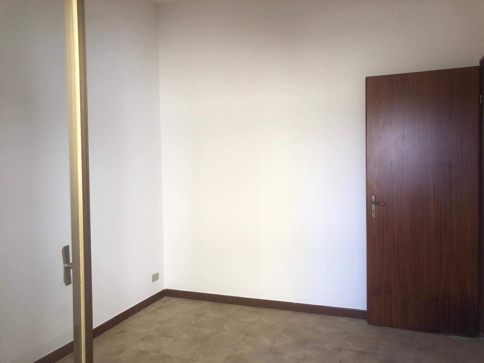 Interni di una stanza vuota con pareti bianche, pavimento in piastrelle e porta in legno scuro, immagine di un appartamento in vendita o affitto.