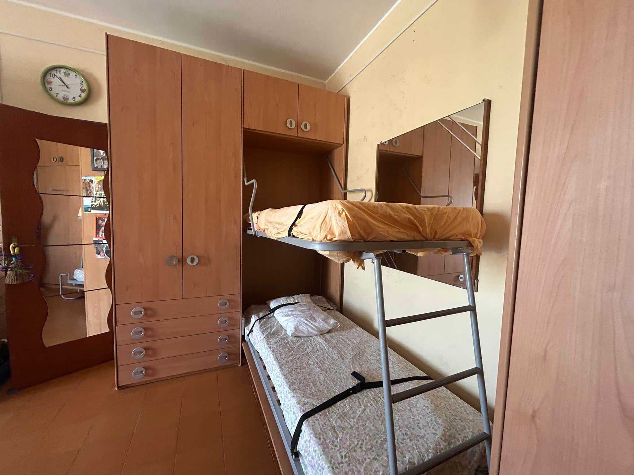 Armadio in legno con letto a castello, stanza da letto ordinata e funzionale, ideale per appartamenti in affitto o studenti, con armadi spaziosi e spazio per relax e studio.