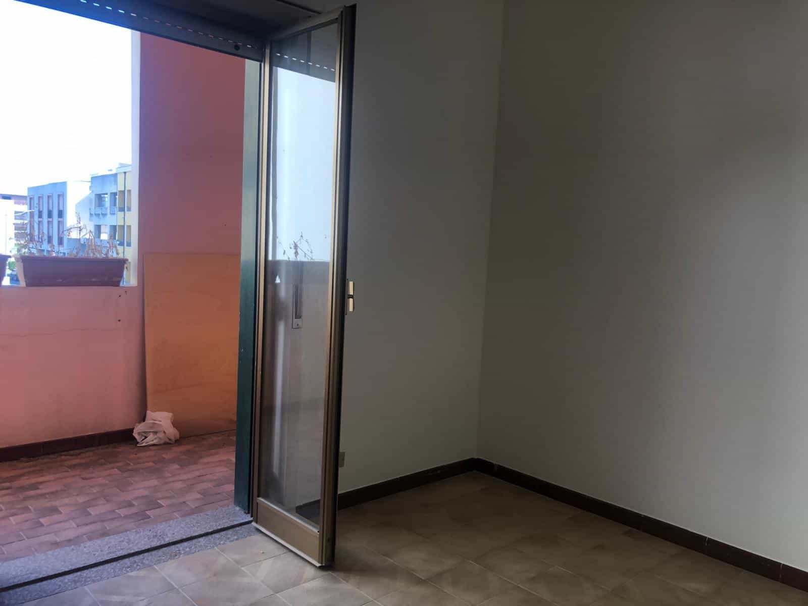 Finestra scorrevole in alluminio che apre su un balcone con vista su edifici residenziali, all’interno di un appartamento moderno, esempio di ristrutturazione e design contemporaneo.