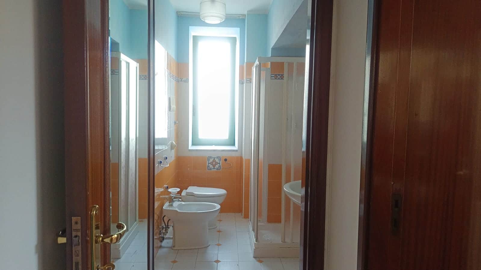 Lavabo e doccia in bagno luminoso con finestra, pavimentazione chiara e dettagli colorati, ideale per appartamenti in vendita o in affitto a Napoli.