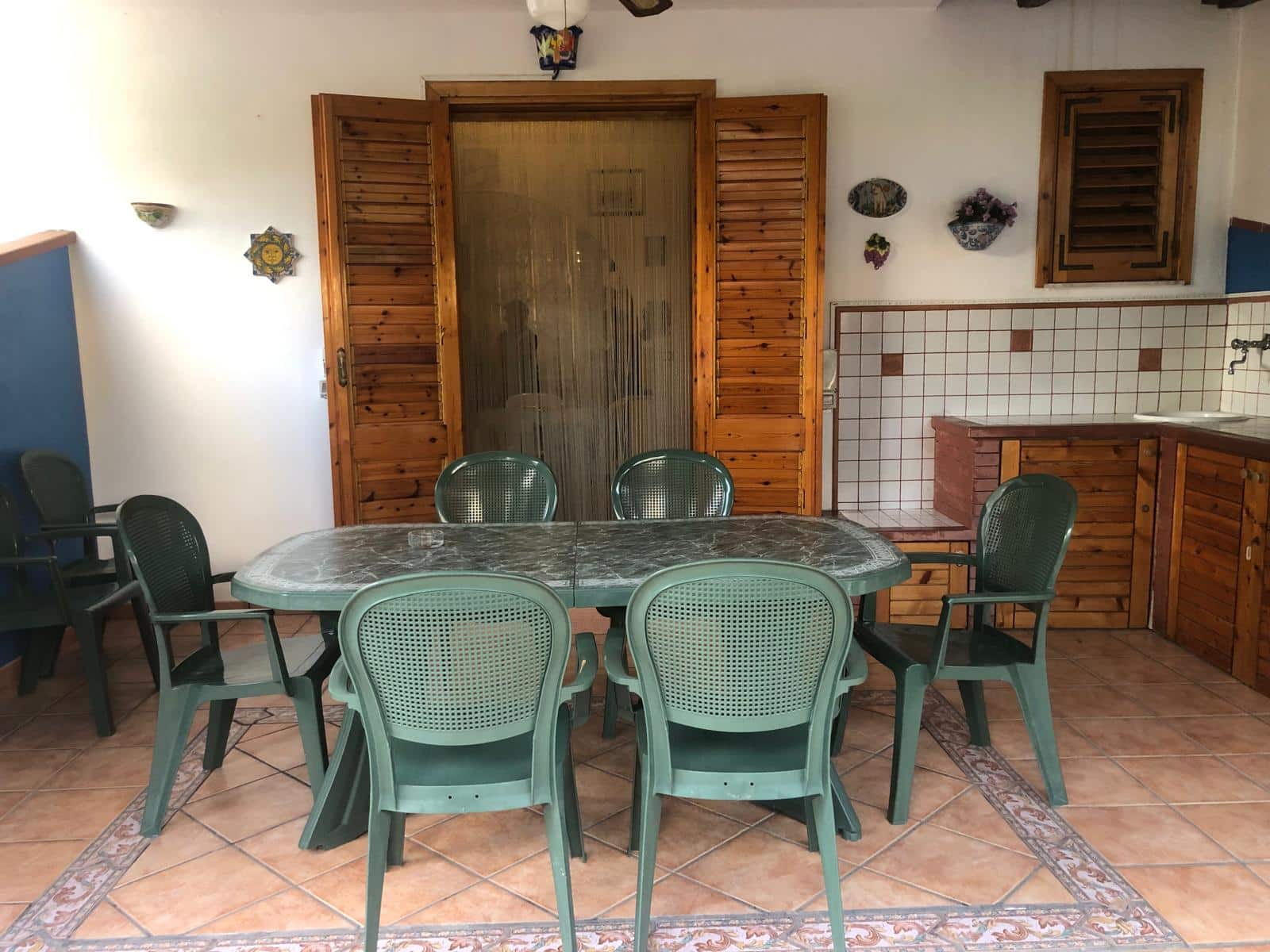 Tavolo da pranzo in marmo con sedie di plastica verdi, cucina in stile rustico con pareti in piastrelle bianche e dettagli in legno, ambiente accogliente e informale.