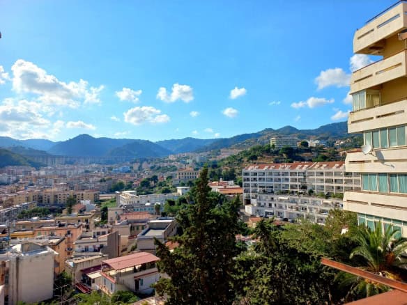 VISTA PANORAMICA di un quartiere residenziale con montagne sullo sfondo, cielo azzurro con nuvole, edifici moderni e zone verdi, vista dal balcone di un appartamento a NextCasa.