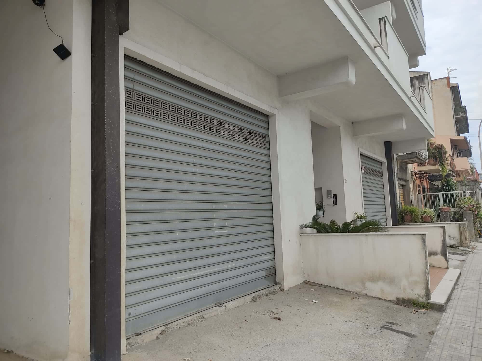Ampia autorimessa con porta basculante in acciaio, situata in zona residenziale vicino a negozi e servizi. Edificio moderno con facciata bianca, ideale per parcheggio sicuro e protezione dei veicoli.