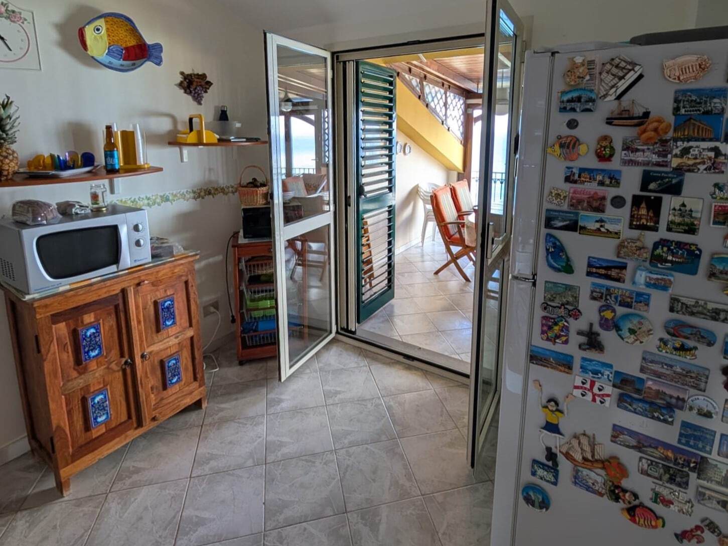 Finestra con balcone che si affaccia sul mare, zona giorno luminosa e accogliente, arredamento utile e colorato, ambiente domestico confortevole e vivace, ideale per vacanze al mare.