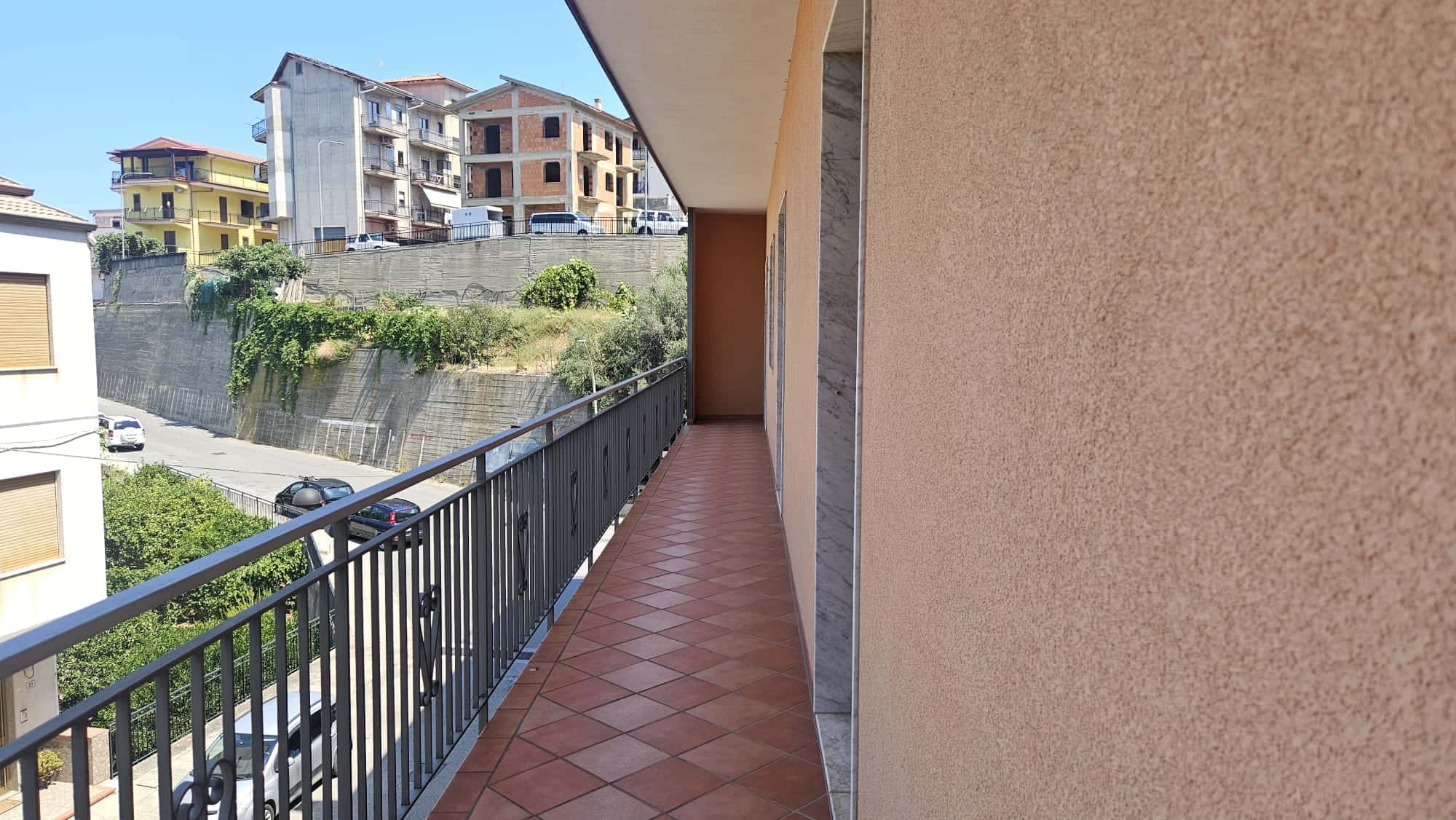 Balcone di un appartamento con vista sulle case e il paesaggio urbano, pavimentazione in ceramica e ringhiera in ferro, ambiente luminoso e spazioso, ideale per abitare o rilassarsi all'aperto.