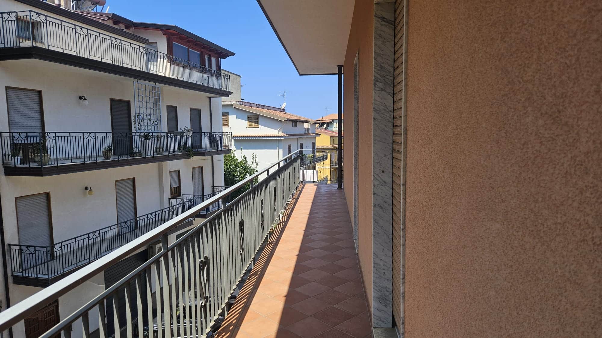 Balcone di un appartamento in zona residenziale con vista sulle altre abitazioni, pavimentazione in ceramica e ringhiera in ferro battuto, ideale per vivere in tranquillità.