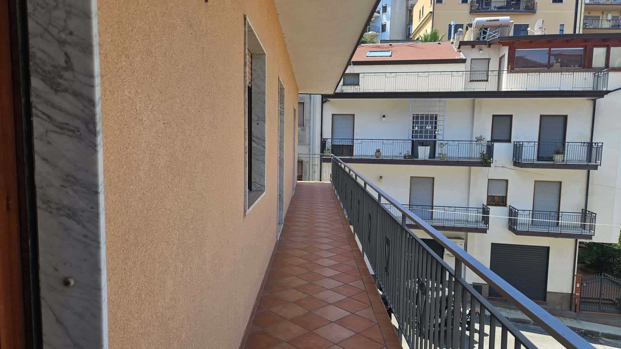Balcone di un appartamento in centro città con ringhiera in metallo e pavimento in gres porcellanato, vista su edifici residenziali e vie della zona.