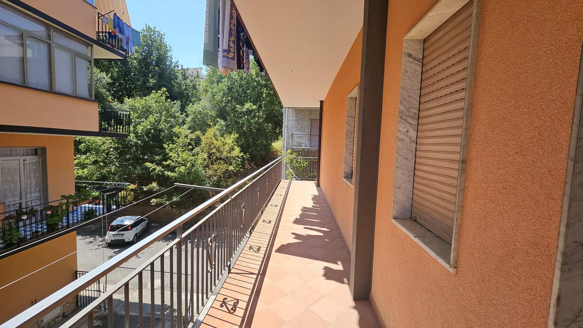 Balcone spazioso con ringhiera in ferro, vista su cortile con piante e altri condomini, ideale per relax e attività all'aperto - NextCasa.
