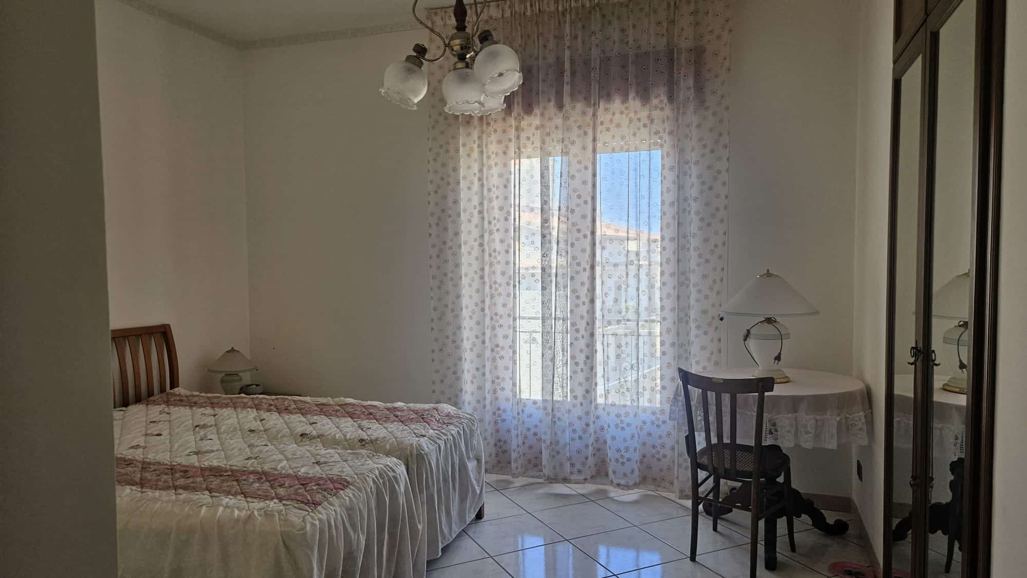 Dormitorio con cama singola e armadio, stanza luminosa con tendaggi leggeri, lampade da tavolo, arredamento classico, ideale per case in affitto, vendita immobili e soluzioni residenziali NextCasa.