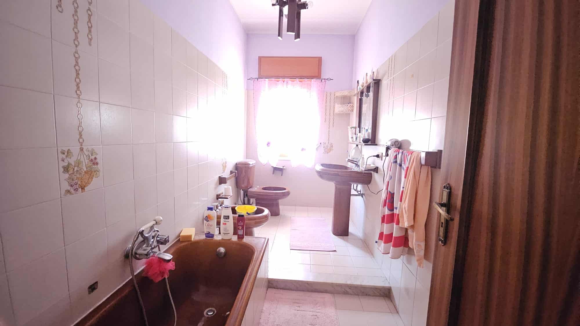 Bagno spazioso con vasca idromassaggio, lavabo e WC, illuminato da luce naturale, con asciugamani e prodotti di bellezza, arredi in stile classico, ideale per comfort e benessere.
