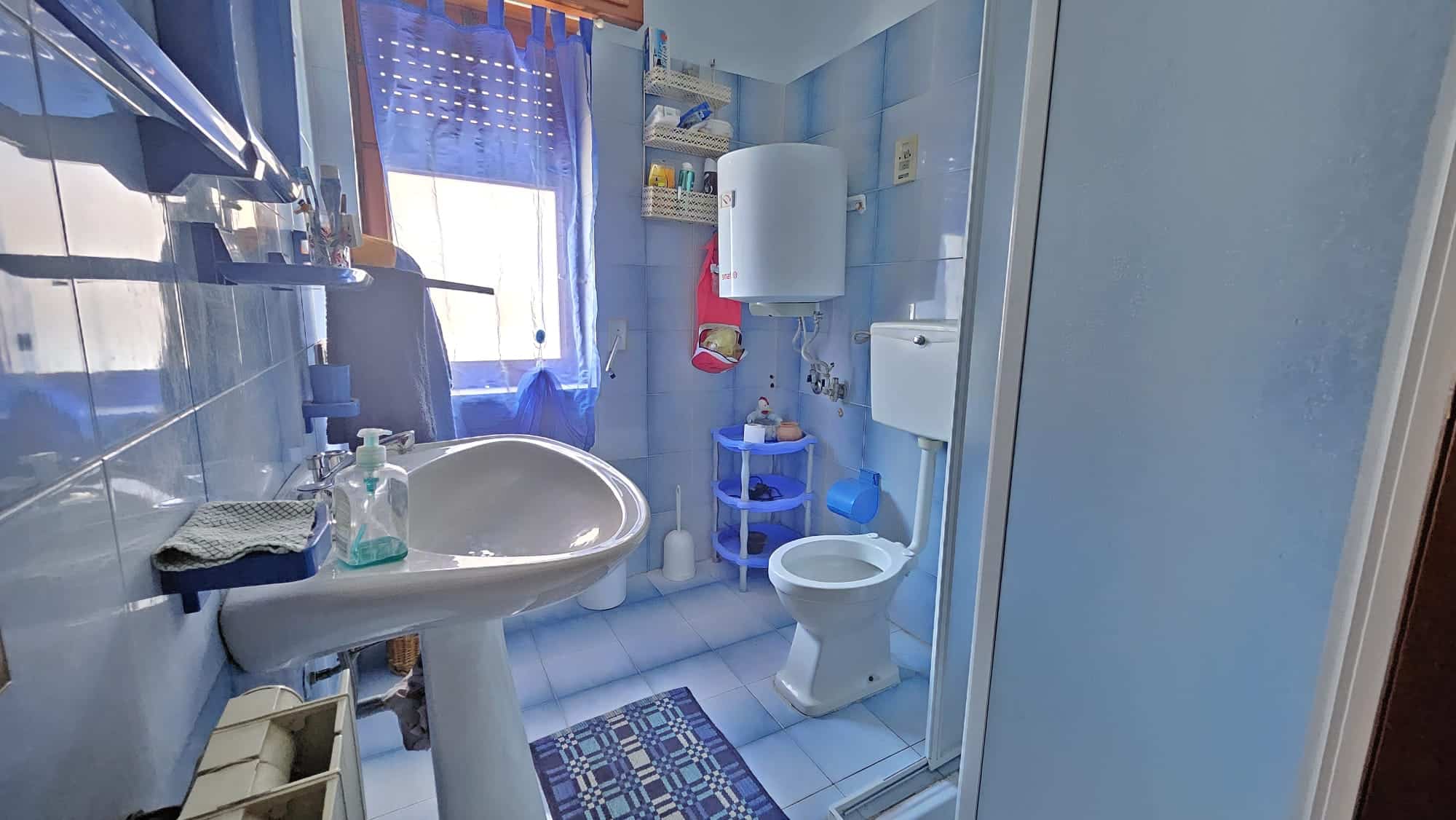 Lavabo e servizi igienici in bagno con piastrelle blu, finestra e arredi funzionali, ambiente domestico, casa accogliente, ristrutturazione bagno, soluzioni di arredo bagno.