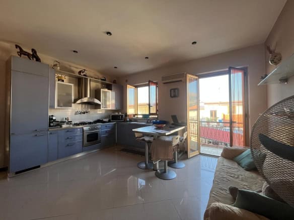 Luminoso soggiorno open space con cucina moderna, finestre grandi e balcone, arredamento confortevole, ideale per vivere in comodità e relax in un ambiente accogliente e luminoso.