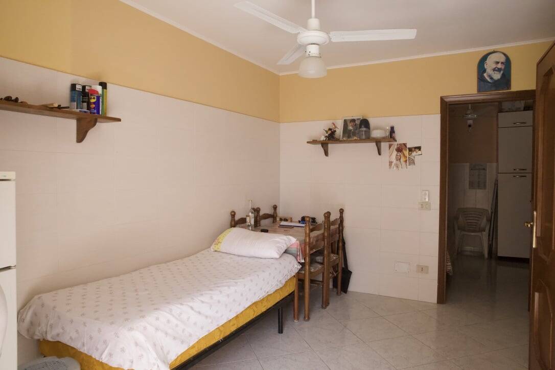 Letto singolo in camera con arredamento semplice, pareti bianche e beige, mensole in legno, moderni elementi di arredo, ideale per abitazioni e affitti turistici.