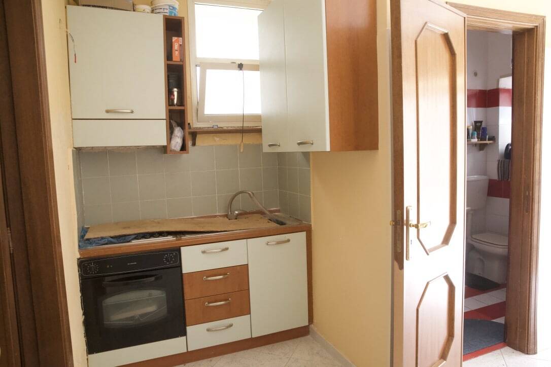 Mini cucina con lavabo e forno integrato, arredamento in legno e bianco, finestra naturale, spazi funzionali, ambiente compatto e pratico per la casa, vista sulla stanza da bagno con sanitari, stile semplice e abitabile.