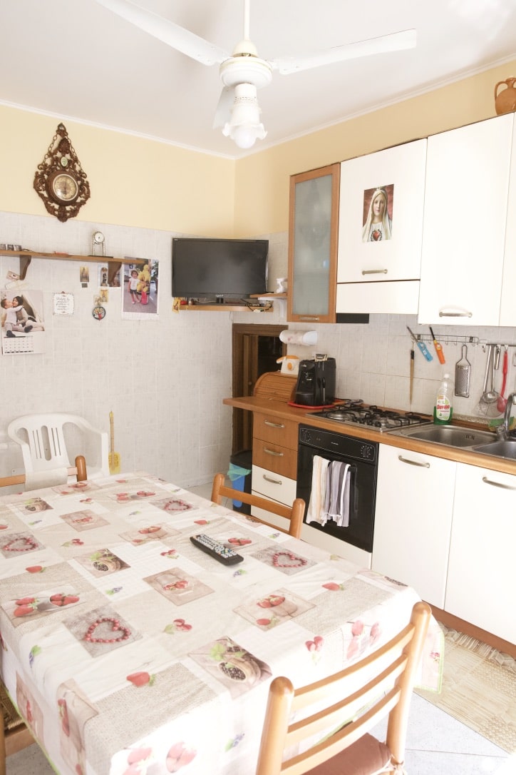 Cucina abitabile con tavolo da pranzo decorato, armadietti bianchi, forno a gas, televisore e accessori cucina, ambiente accogliente e funzionale, ideale per la vita quotidiana.