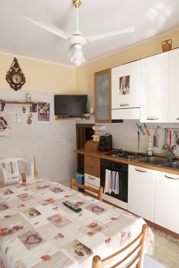 Cucina abitabile in stile tradizionale con mobili bianchi e altezza porta in legno, tavolo da pranzo con tovaglia decorata, elettrodomestici e decorazioni rustiche.